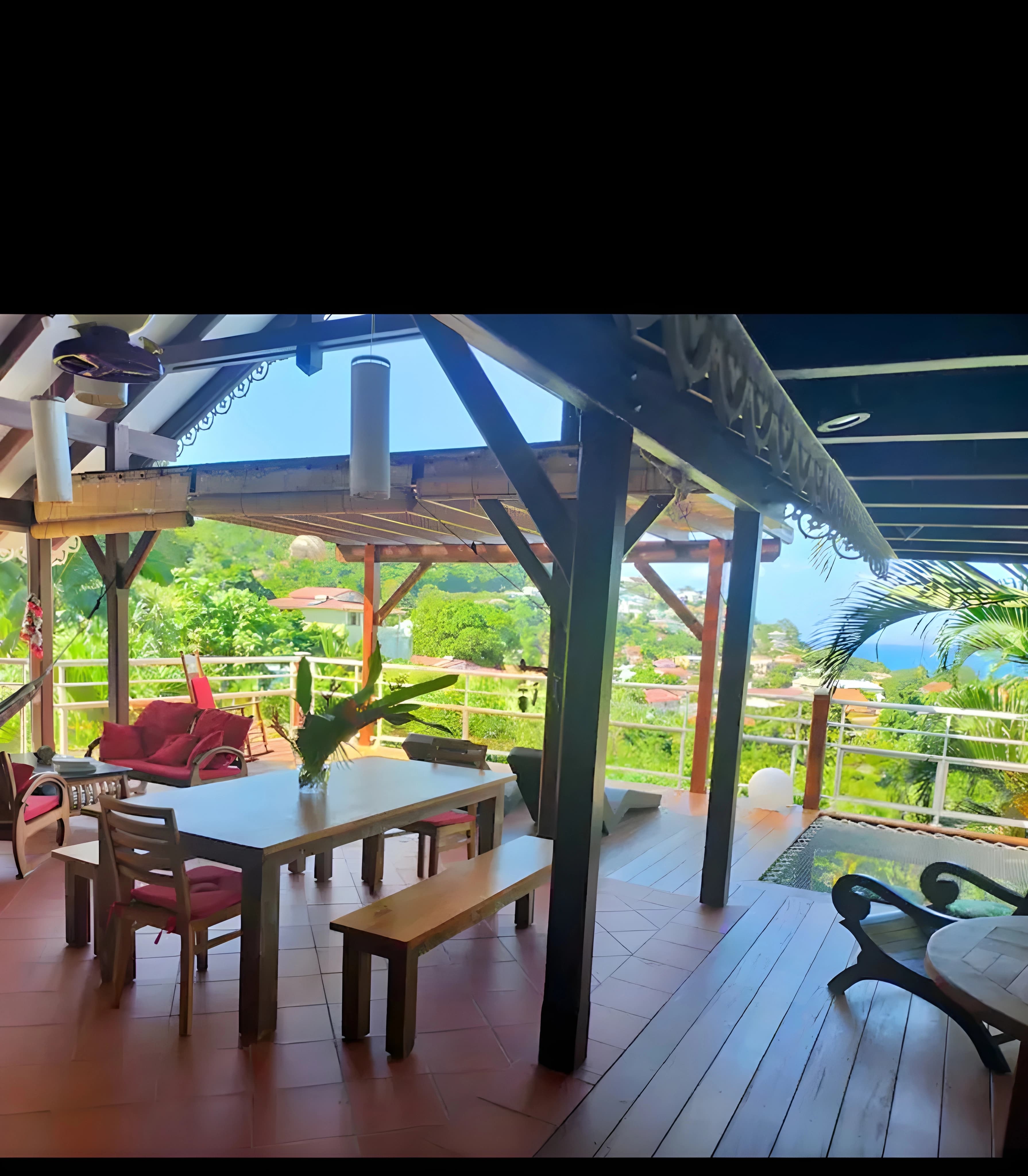 Terrasse couverte en bois avec table, bancs et transat sous charpente créole