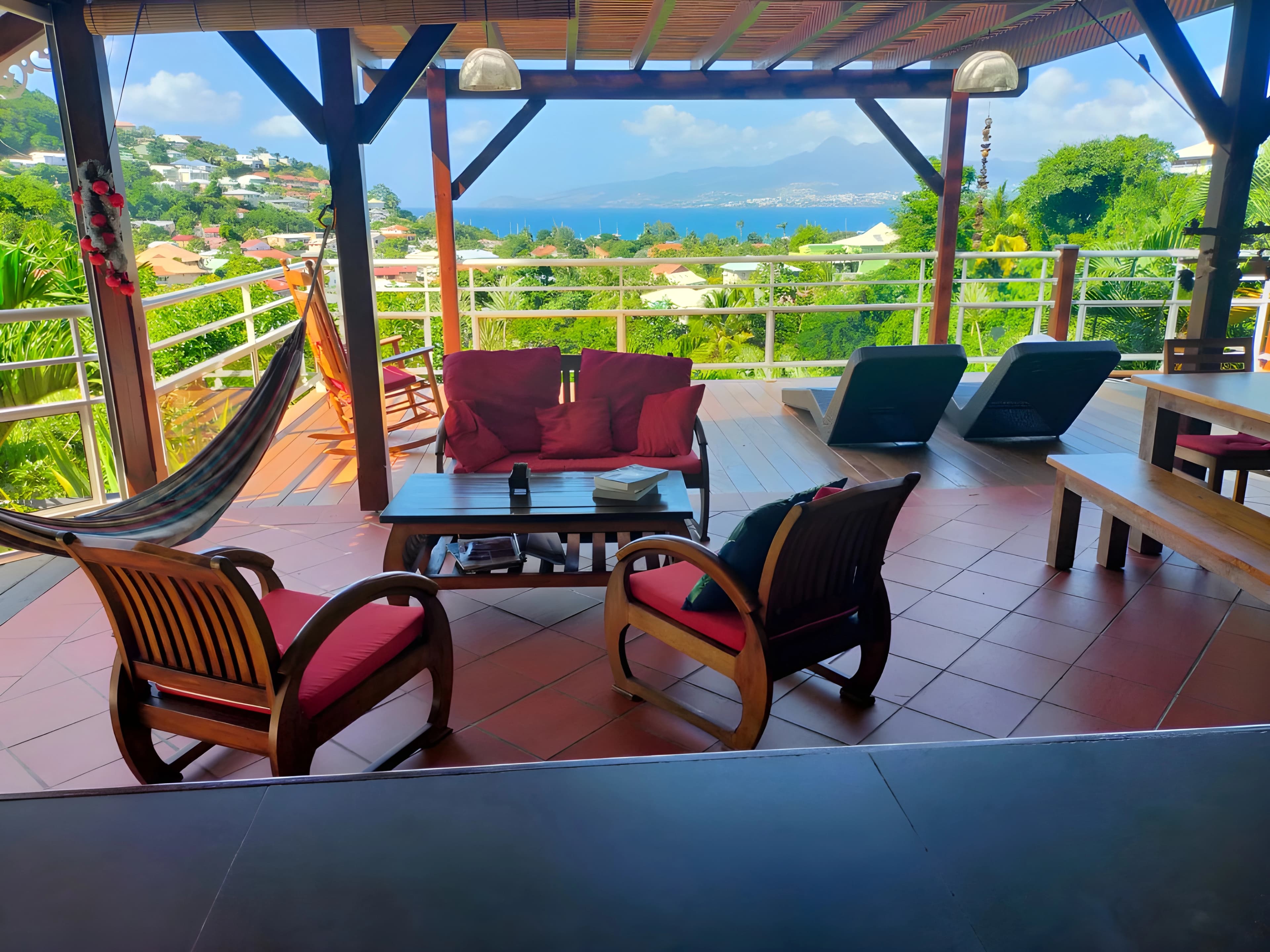 Grande terrasse avec hamac, fauteuils créoles et transats face à la baie