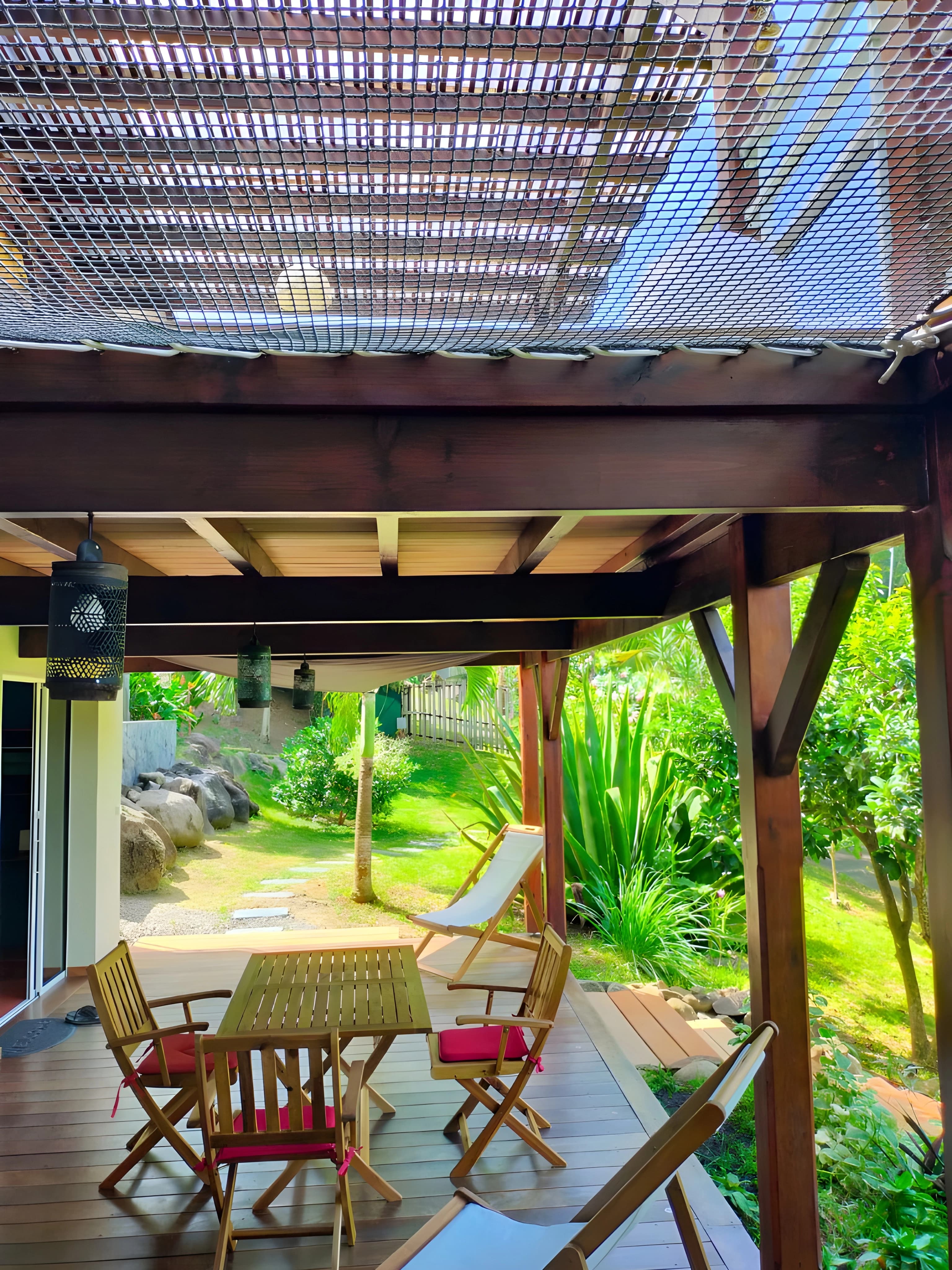 Coin repas extérieur en bois sous pergola pour le studio, ouvert sur le jardin