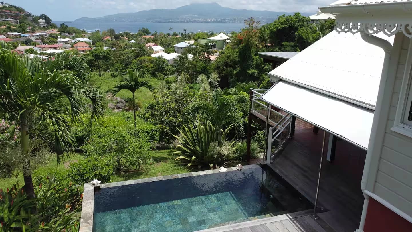 Vue plongeante sur la piscine, le jardin tropical et la villa, baie au fond