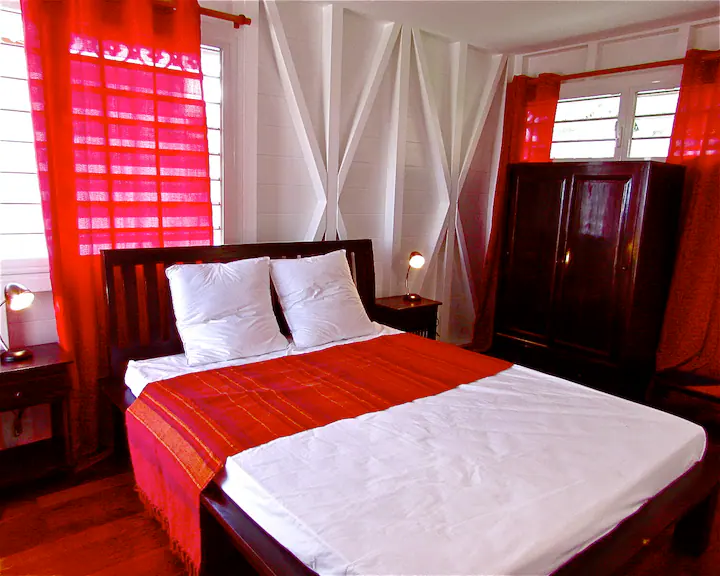 Chambre principale avec lit double, tête de lit en bois, voilages et moustiquaire